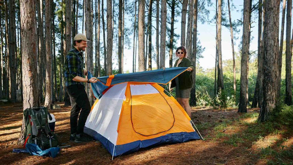 Två personer som sätter upp ett tält på en camping i skogen