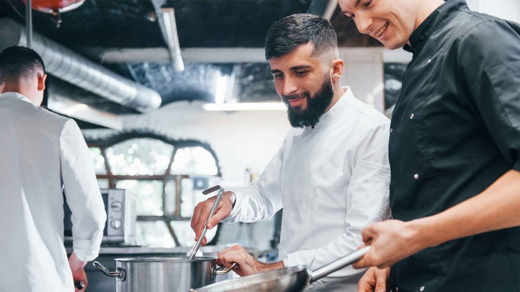 Tre personer som står i ett kök och lagar mat i ett restaurangkök